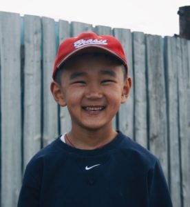 boy in blue crew neck shirt and red cap smiling