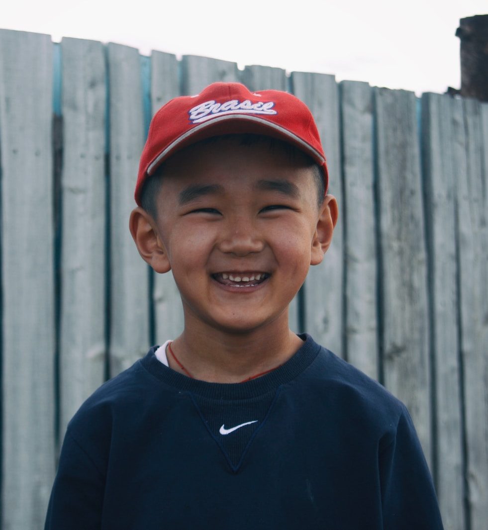 boy in blue crew neck shirt and red cap smiling